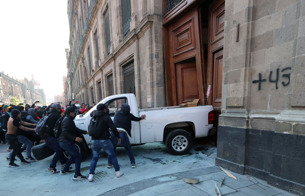 Manifestantes empujan una camioneta para derribar la puerta del palacio presidencial en la Ciudad de México el 6 de marzo de 2024, durante una protesta por la desaparición de los 43 estudiantes de la escuela de formación docente de Ayotzinapa en 2014. (Foto de VALENTINA ALPIDE/AFP vía Getty Images).